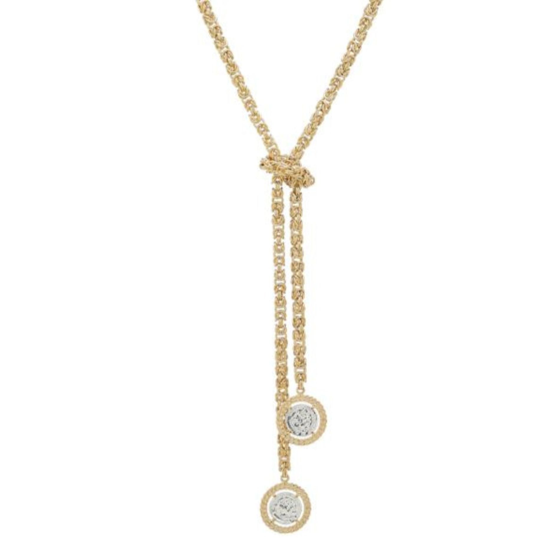 Stylish gold necklace featuring a central knot and two strands that end in circular coin-like pendants, showcasing a silver design within a textured gold frame.